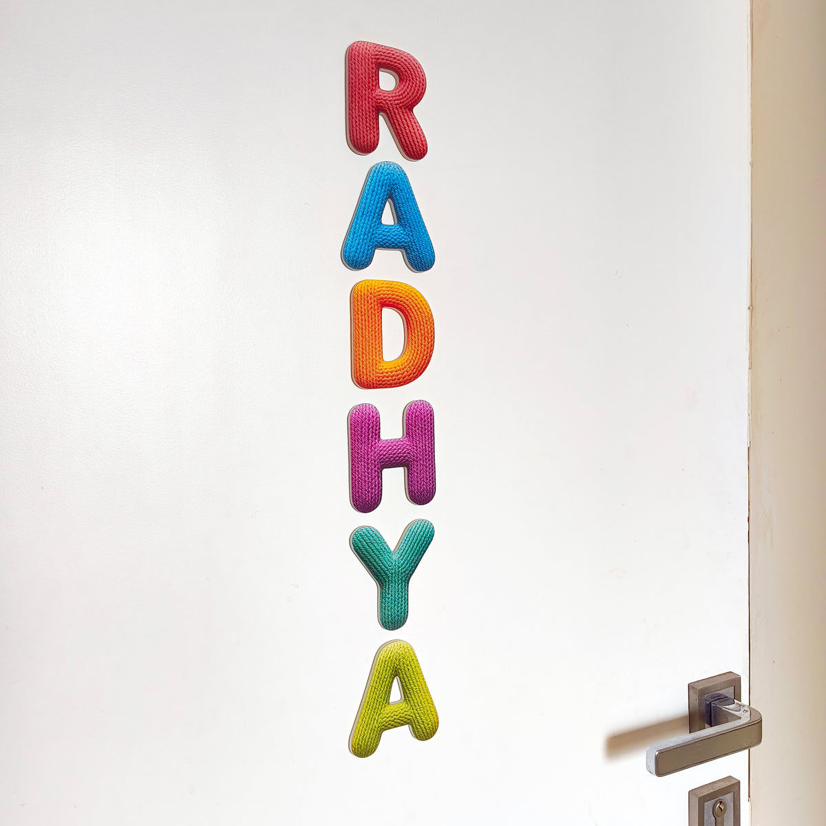Colorful knit letters spelling 'RADHYA' on a white door.