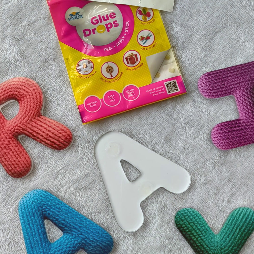 Colorful letter-shaped objects with a package of 'Glue Drops' on a gray surface